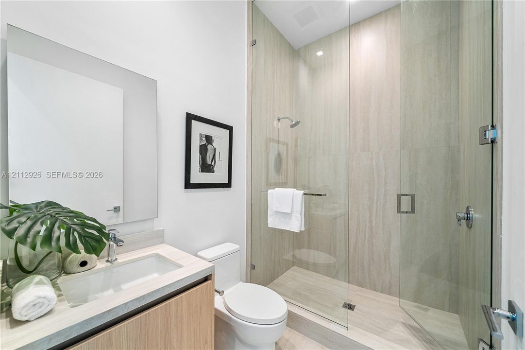 Bathroom featuring a floating vanity with a stone countertop, an integrated rectangular sink, a frameless glass-enclosed shower with floor-to-ceiling neutral tile, and a wall-mounted mirror