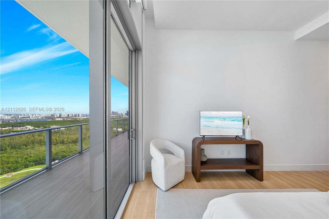 Floor-to-ceiling sliding glass door, private balcony with metal railing, and wood-finish flooring