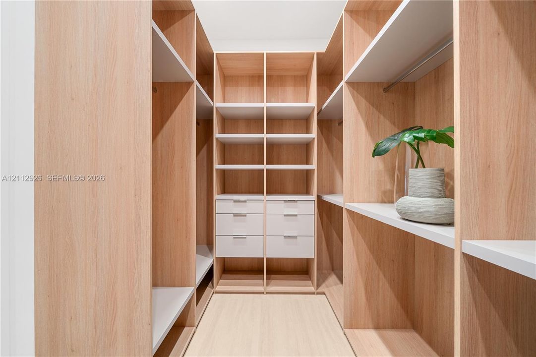 Custom walk-in closet featuring light wood-finish cabinetry, floor-to-ceiling shelving, integrated hanging rods, and built-in drawers with modern pulls