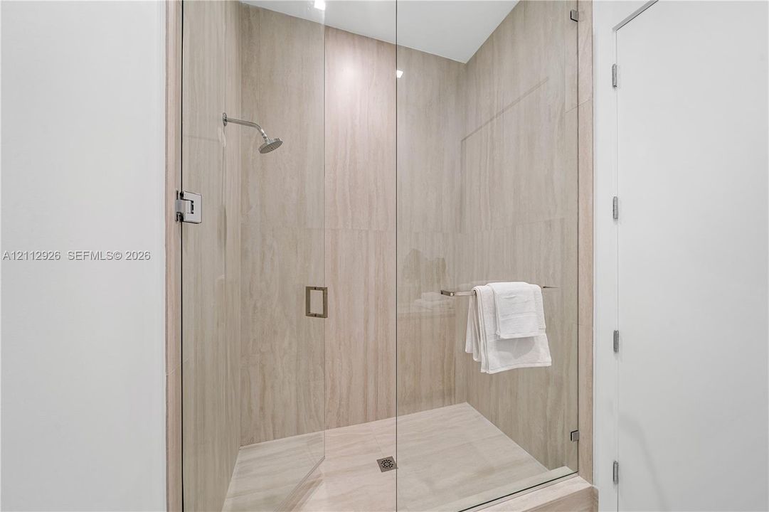 Walk-in shower featuring floor-to-ceiling neutral-toned tile, a frameless glass enclosure, and a fixed shower head