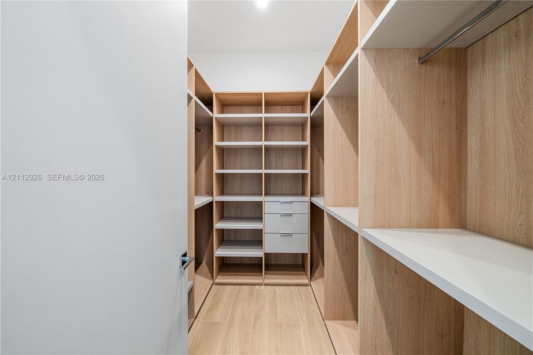 Custom walk-in closet featuring wood-finish cabinetry, built-in shelving, integrated drawers, metal hanging rods, and wood-finish flooring