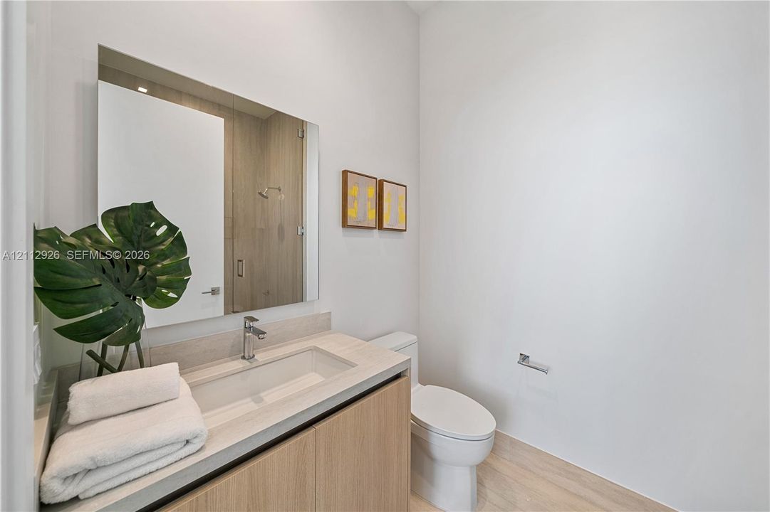 Floating vanity with wood-finish cabinetry, rectangular integrated sink, polished chrome faucet, and frameless wall-mounted mirror