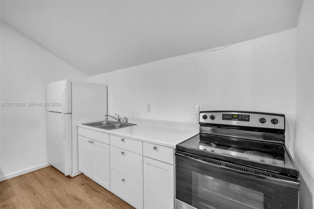 Kitchenette featuring white cabinetry, solid-surface countertops, a stainless steel dual-basin sink, a freestanding electric range, and wood-finish flooring