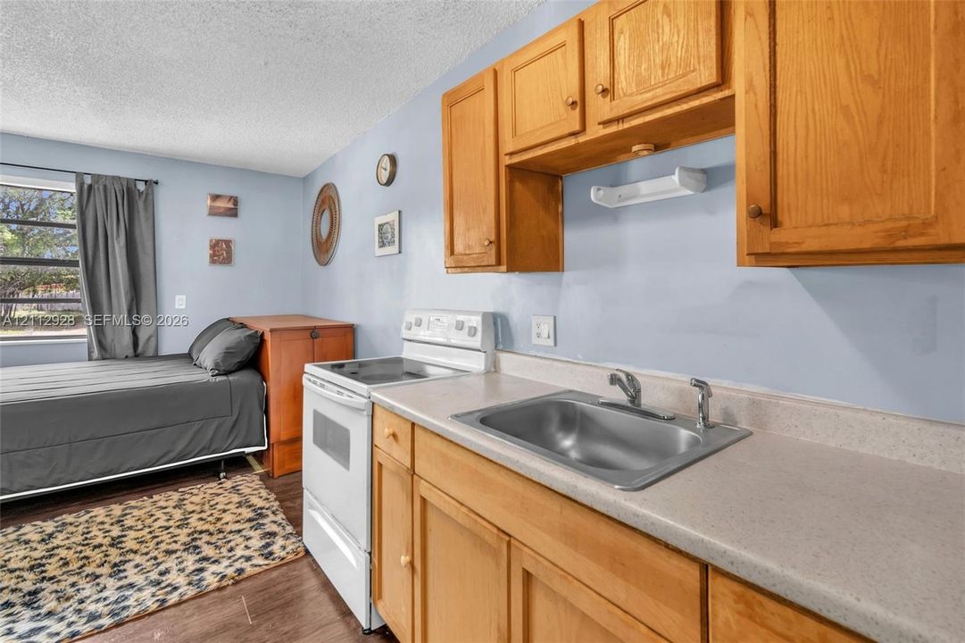Kitchenette featuring wood-finish cabinetry, solid-surface countertops, a stainless steel sink with a dual-handle faucet, and an electric range
