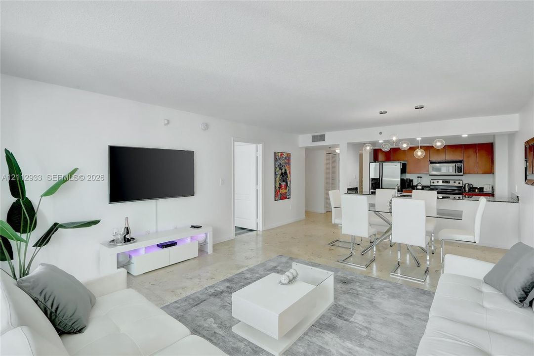 Open-concept living space featuring natural stone flooring, kitchen with wood-finish cabinetry, and contemporary multi-pendant lighting