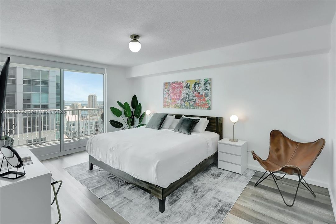 Floor-to-ceiling glass sliding doors opening to a private balcony, wood-finish flooring, and a globe-style flush mount ceiling light fixture