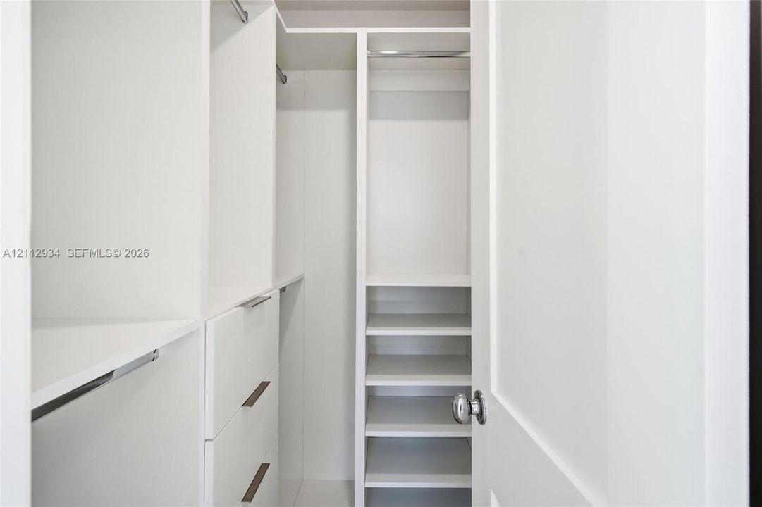 Custom storage system featuring white cabinetry, integrated shelving, tiered drawer banks, and metal hanging rods