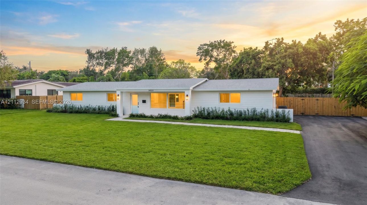 Single-story residence featuring a white horizontal siding exterior, low-pitch roof, concrete walkway, expansive front lawn, and paved side driveway