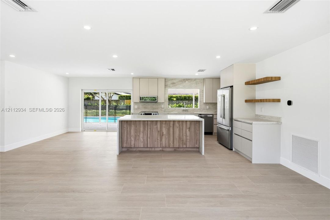 Kitchen featuring a central island with wood-finish cabinetry, stone countertops, stainless steel appliances, and floating shelves