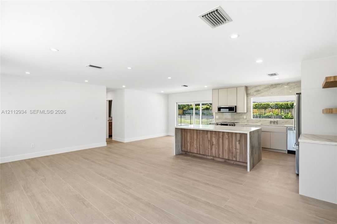 Open-concept kitchen featuring an island with wood-finish cabinetry, light-toned stone-finish countertops, recessed lighting, and wood-finish flooring
