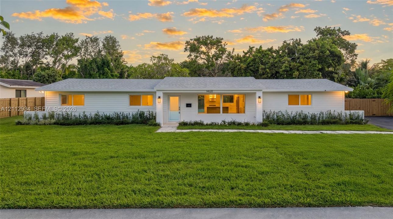 Single-story residence featuring white horizontal siding, a light-toned shingle roof, expansive front lawn, and natural wood-finish privacy fencing