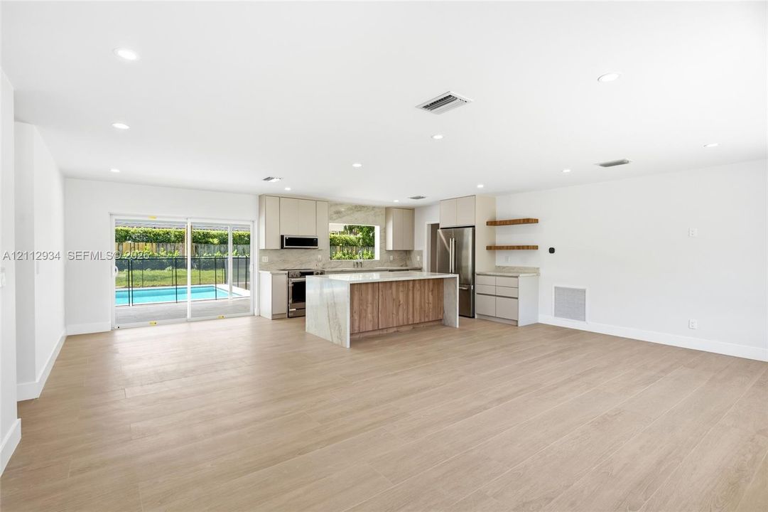 Open-concept kitchen featuring an island with stone-finish waterfall countertop, wood-finish cabinetry, stainless steel appliances, recessed lighting, and wood-finish flooring