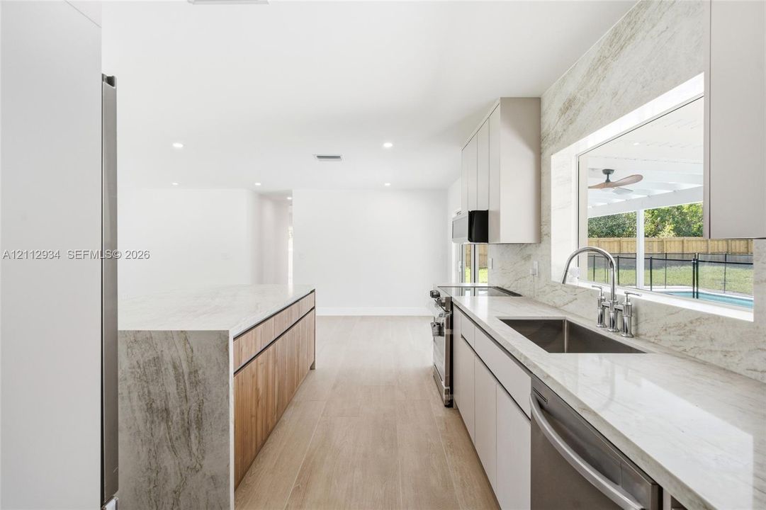 Kitchen featuring stone-finish countertops and full-height waterfall island, wood-finish cabinetry, stainless steel undermount sink with gooseneck faucet, and wood-finish flooring