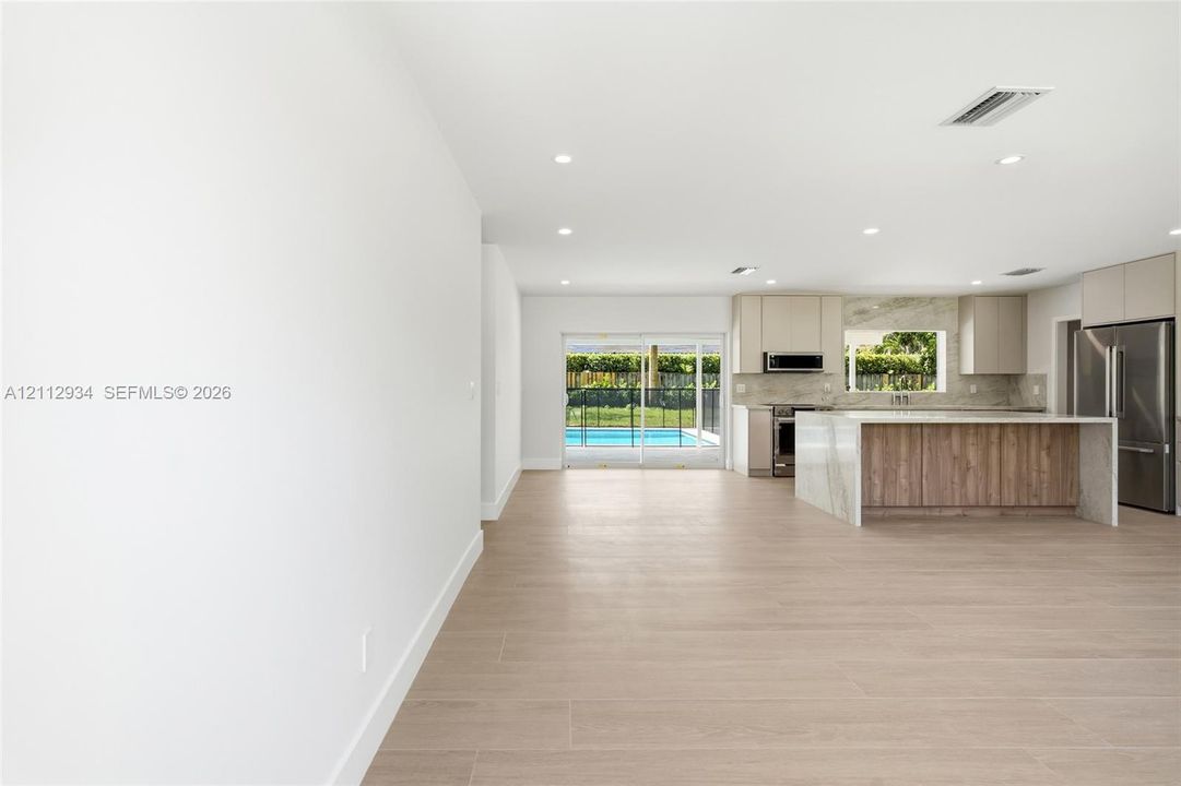 Open-concept kitchen featuring an island with a waterfall-edge stone countertop, wood-finish cabinetry, recessed lighting, and wood-finish flooring, with sliding glass doors leading to a pool area