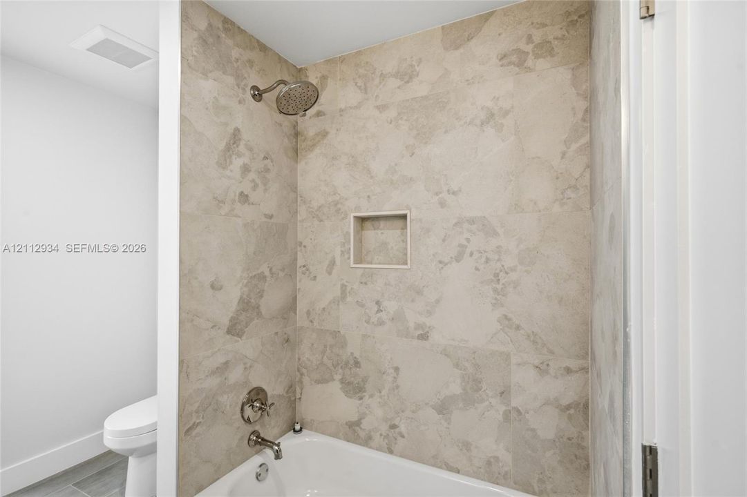 Full-height shower surround with neutral-toned tile, built-in recessed storage niche, and polished metal plumbing fixtures