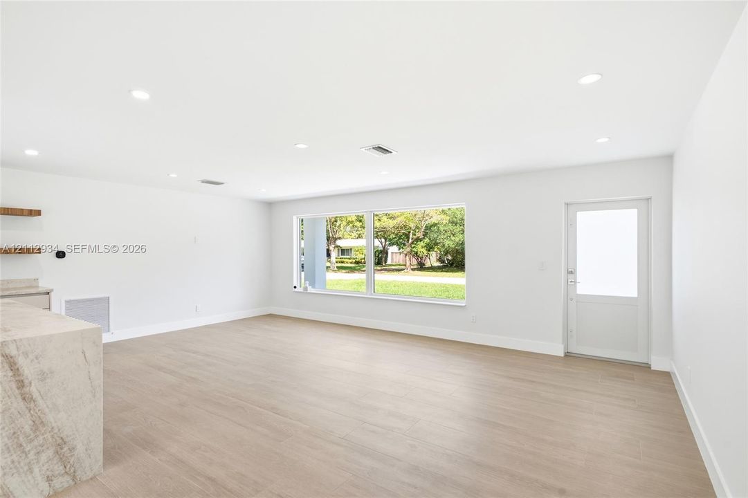 Open-concept space featuring wood-finish flooring, recessed lighting, expansive picture window, natural stone-topped built-in cabinetry, and a glass-paneled exterior door