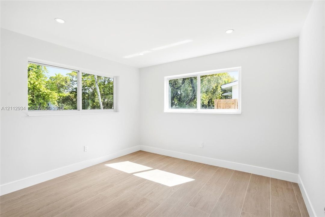 Neutral-toned interior space featuring wood-finish flooring, recessed lighting, and multiple sliding windows