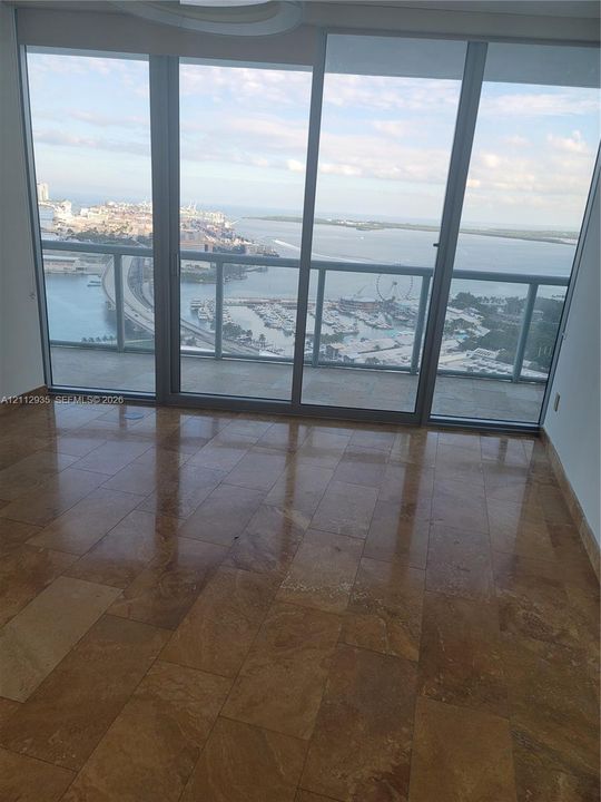 Floor-to-ceiling glass sliding doors, polished stone tile flooring, and a private balcony featuring a metal railing