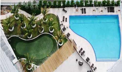 Outdoor recreation area featuring a large swimming pool, a custom putting green, stone-paver decking, and a raised wood-finish walkway surrounded by manicured landscaping and container palm trees