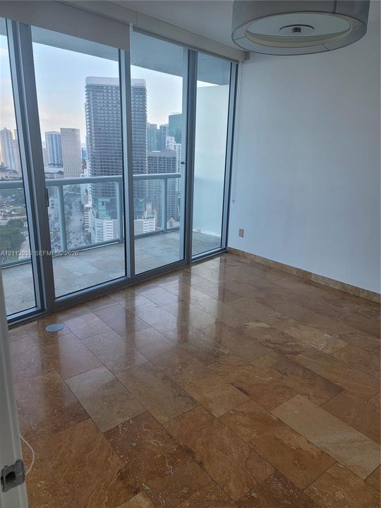 Floor-to-ceiling glass panel walls, natural stone tile flooring, private balcony with metal railing, and circular ceiling-mounted lighting fixture