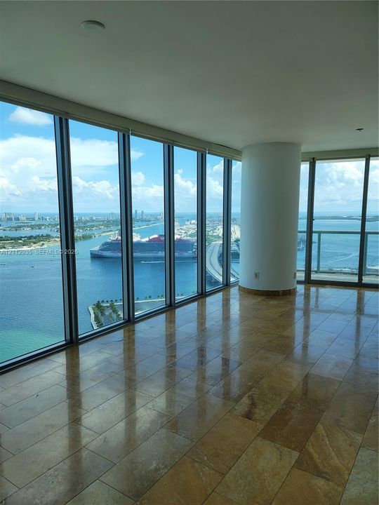 Floor-to-ceiling glass windows, stone tile flooring, and open-concept layout featuring a structural support pillar and an exterior balcony
