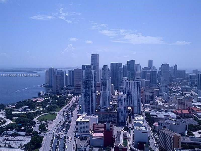 High-altitude cityscape featuring an expansive coastal horizon, dense urban skyline, and waterfront parklands