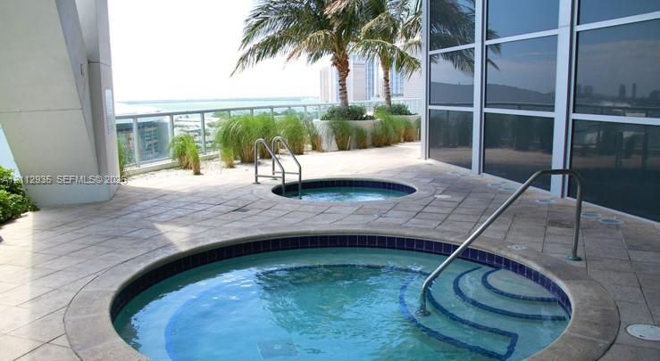 Two inset jetted spas featuring tile surrounds and metal handrails, set within a paved terrace with glass perimeter railing and integrated landscaping