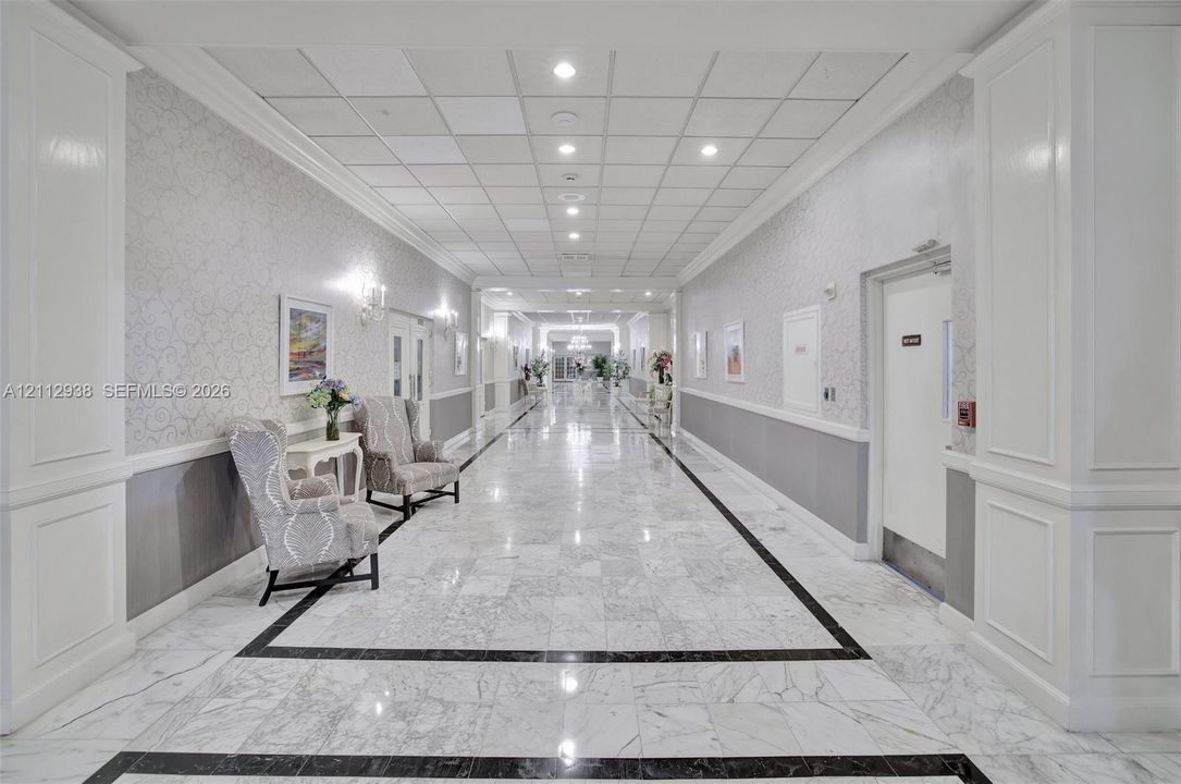 Hallway featuring polished stone flooring with decorative inlay, wall molding, neutral wallpaper, and recessed ceiling lighting