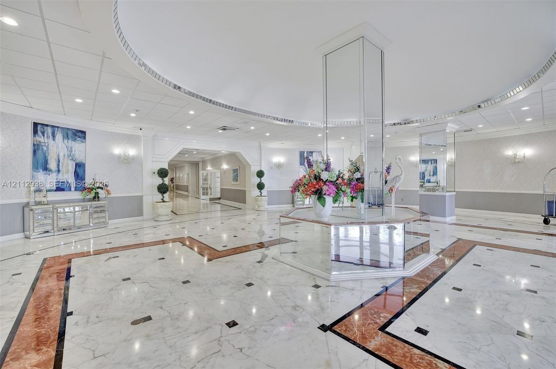 Grand lobby featuring stone flooring with intricate inlay borders, a mirrored central pillar, recessed lighting, and crown molding
