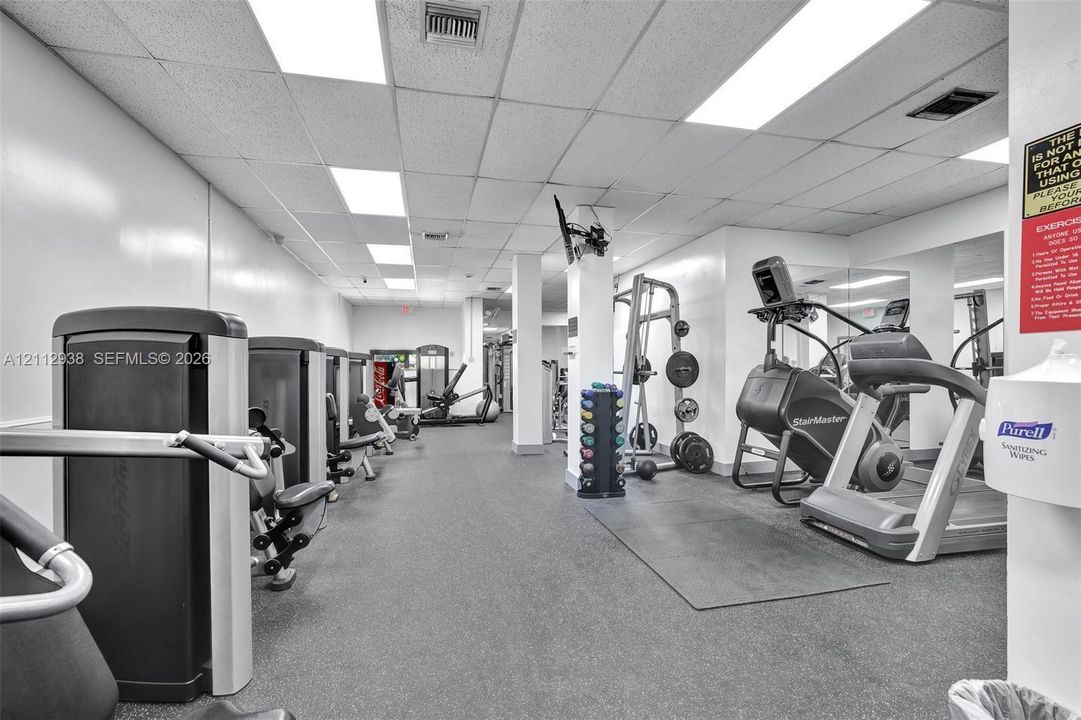 Fitness center featuring rubber flooring, recessed drop-ceiling lighting, and wall-to-wall mirrored surfaces