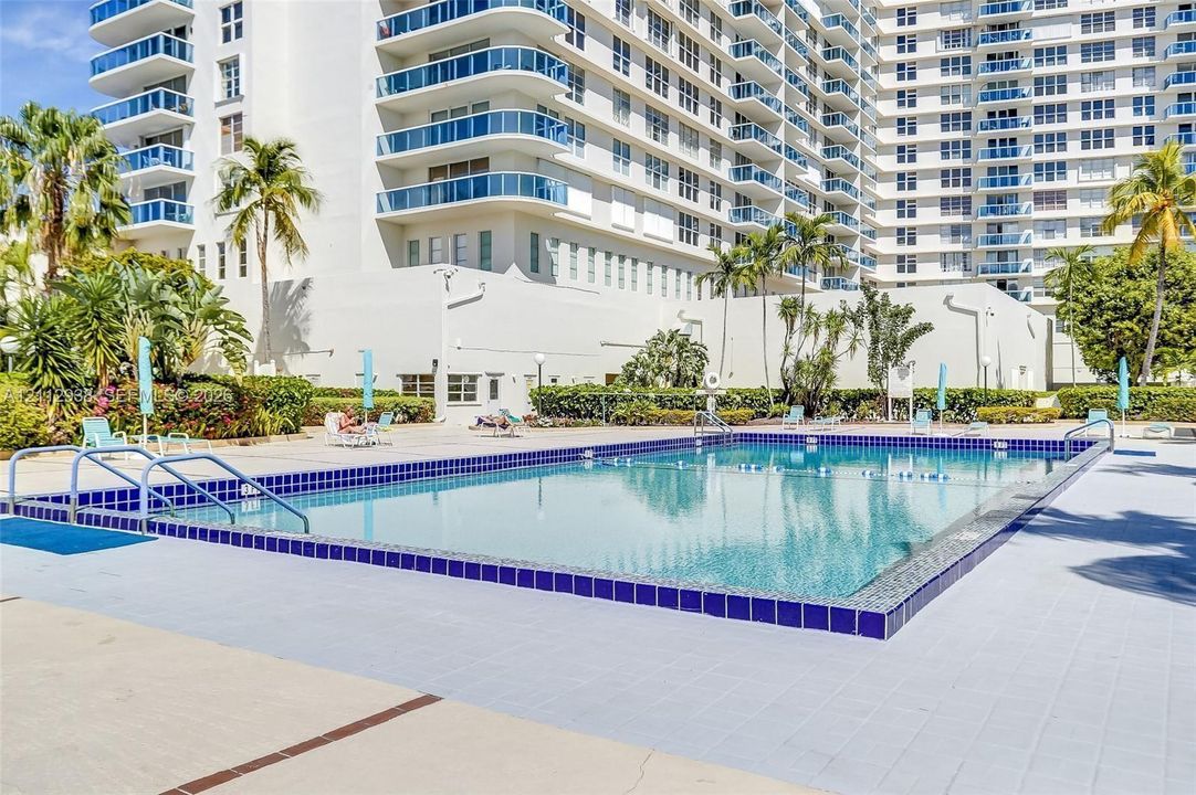 In-ground swimming pool with a tiled perimeter, surrounded by a paved deck, mature palm trees, and professional landscaping