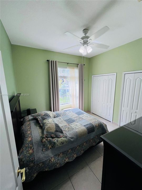 Room featuring tile flooring, dual bi-fold closet doors, and a ceiling-mounted light fixture with a fan