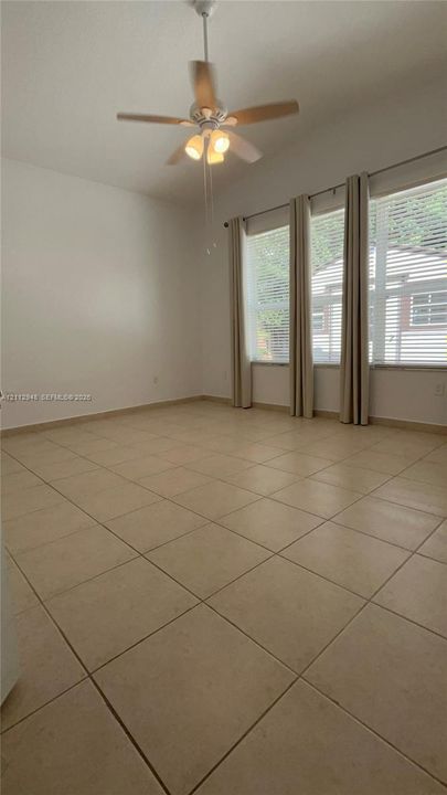Neutral-toned tile flooring, high ceilings, ceiling fan with integrated lighting, and a series of windows with horizontal blinds