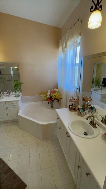 Dual-sink vanity with white cabinetry, solid surface countertops, recessed oval sinks, and a built-in corner soaking tub with tile surround