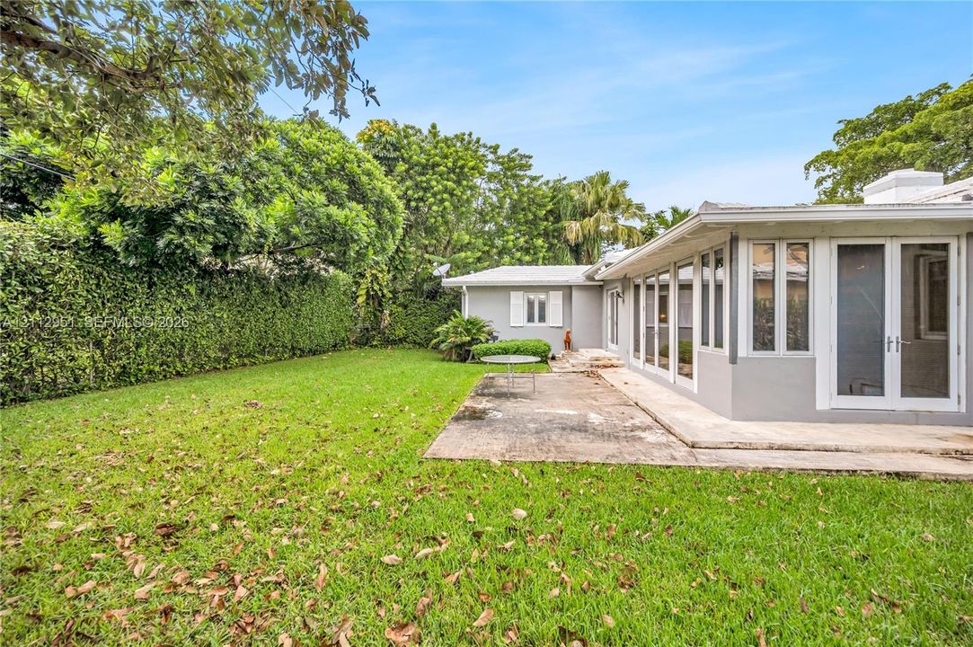 Rear exterior featuring a concrete patio, full-height glass-paneled exterior doors, a grass lawn, and mature perimeter landscaping