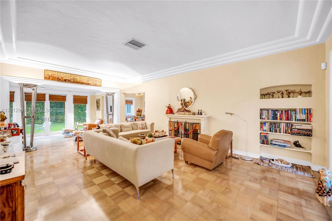 Parquet wood-finish flooring, vaulted ceilings with crown molding, integrated wall shelving, a fireplace with a decorative mantel, and floor-to-ceiling glass panel doors