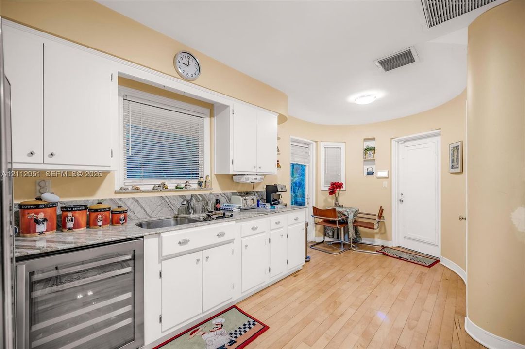 Kitchen featuring white cabinetry, stone countertops, an integrated wine refrigerator, curved wall architecture, and light-toned wood-finish flooring