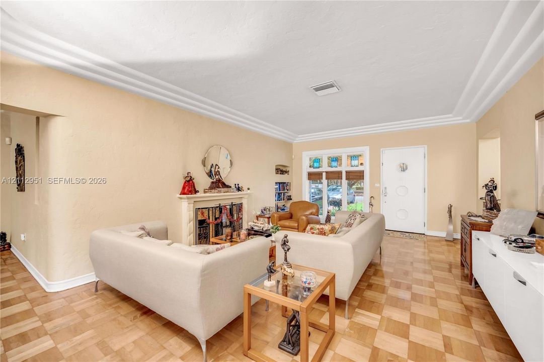 Parquet wood flooring, crown molding, stone fireplace surround, and recessed entryway door with integrated circular glass accents