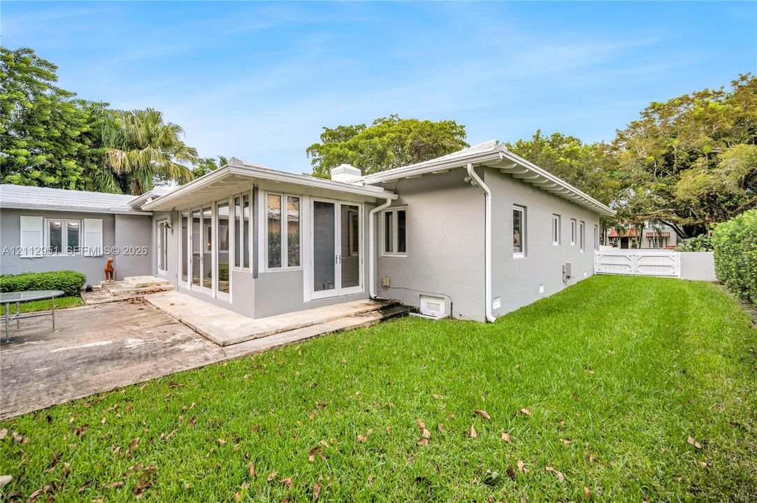 Exterior featuring a light-colored stucco finish, a covered patio with glass-enclosed walls, concrete hardscaping, and a fenced yard with mature trees