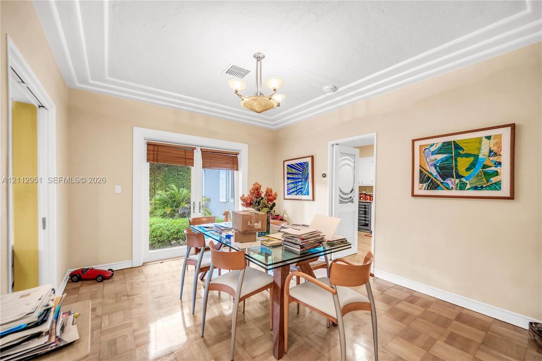 Parquet wood-finish flooring, multi-tiered tray ceiling, multi-light central chandelier, and French glass doors