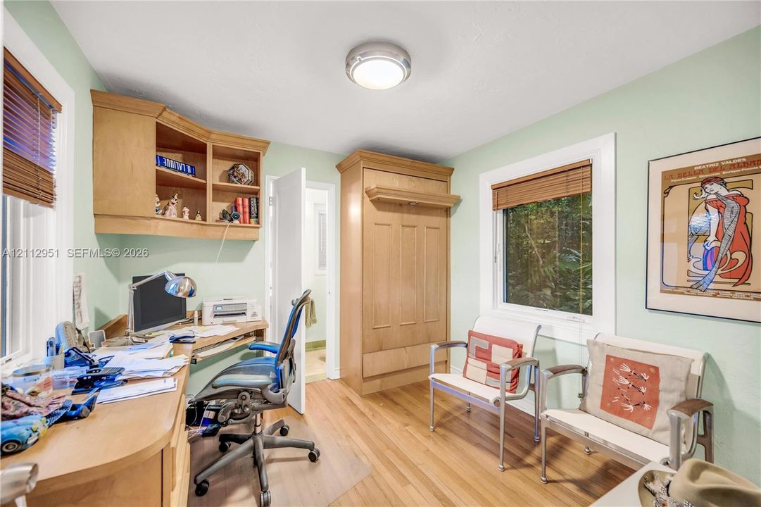 Built-in wood cabinetry, integrated desk workspace with overhead shelving, wall-mounted murphy bed unit, and wood-finish flooring