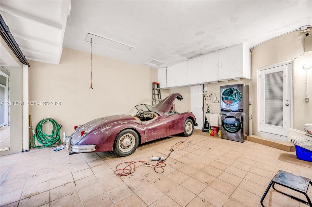 Enclosed garage featuring tile flooring, white built-in upper cabinetry, and a dedicated laundry area with stacked washer and dryer unit