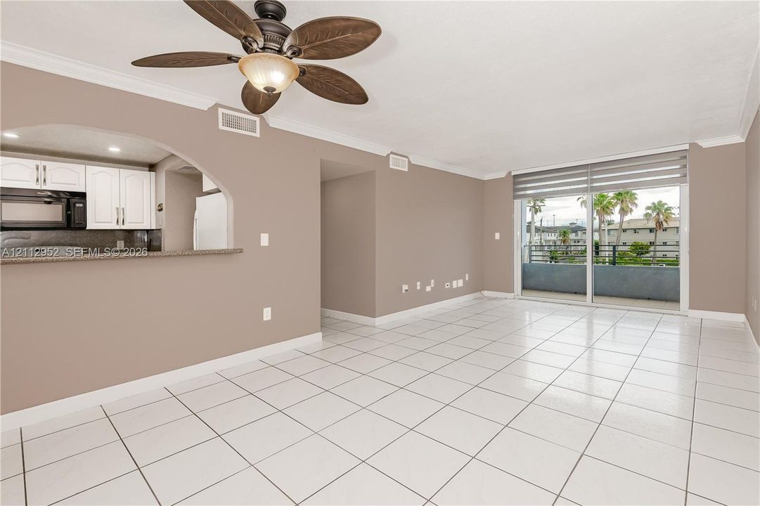 Open-concept interior featuring white tiled flooring, arched wall detailing, a ceiling fan with integrated lighting, and sliding glass doors with horizontal blinds