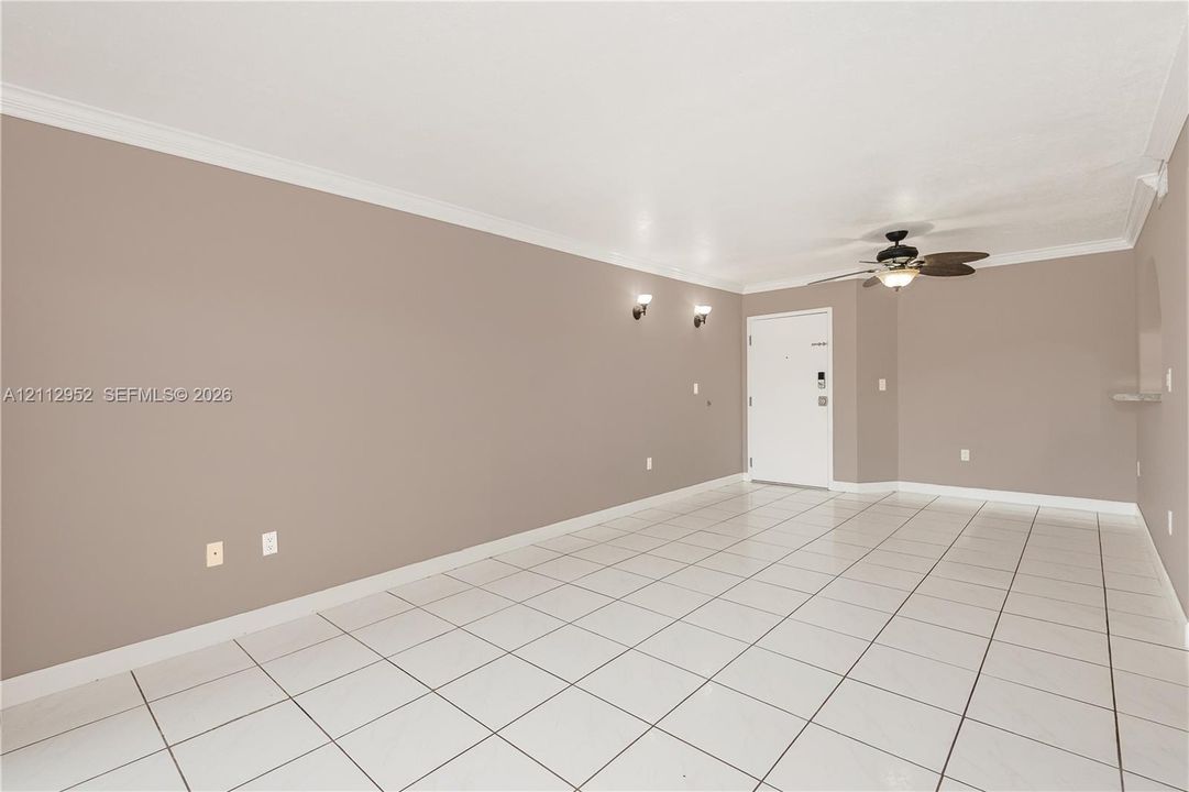 Neutral-toned interior featuring large-format ceramic tile flooring, crown molding, wall-mounted light fixtures, and an integrated ceiling fan