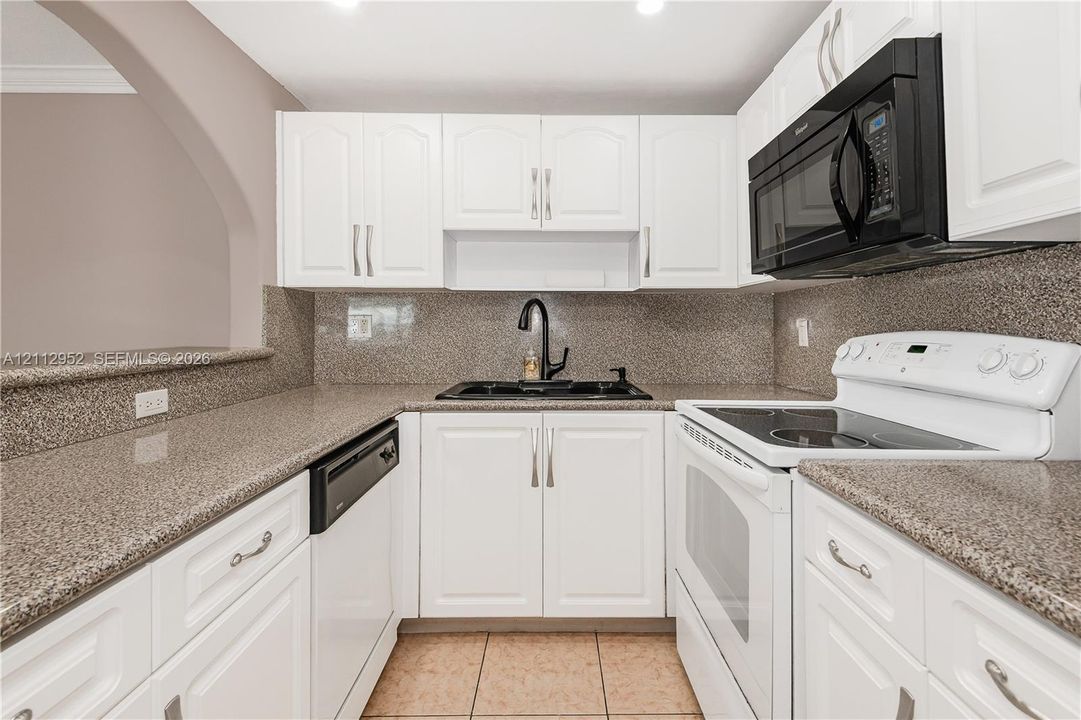 Kitchen featuring white cabinetry, stone-surface countertops, tile flooring, and an arched architectural opening