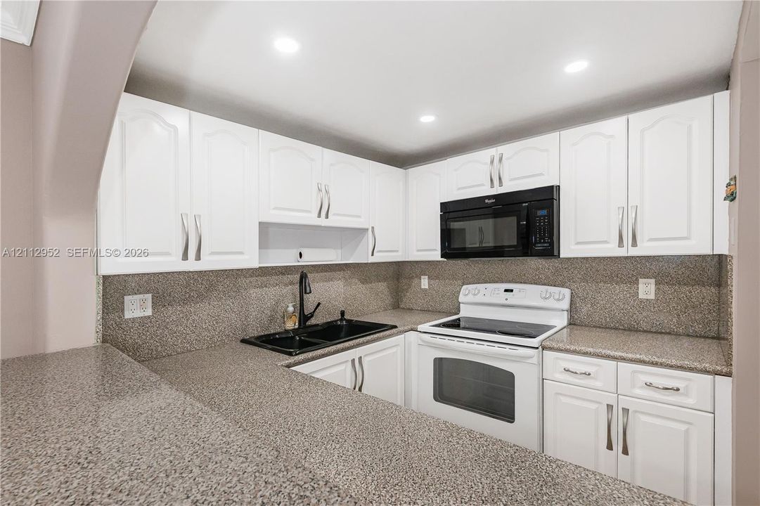 Kitchen featuring white cabinetry with brushed metal pulls, speckled stone-finish countertops, black dual-basin sink, and integrated black microwave