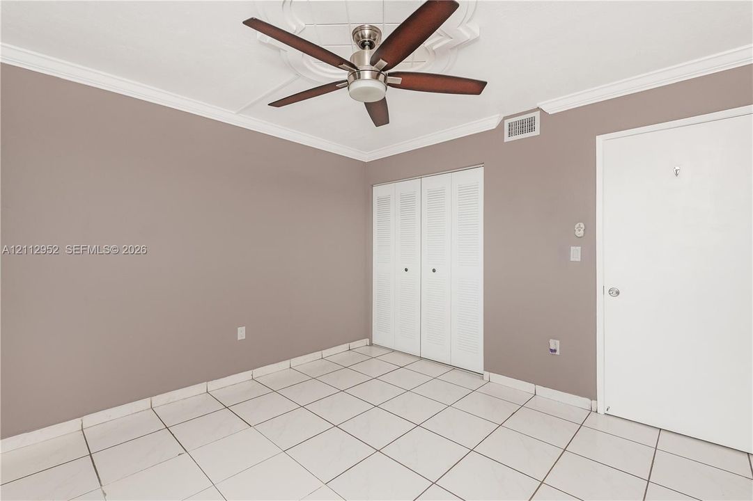 Interior space featuring white ceramic tile flooring, a decorative ceiling medallion, a ceiling fan with wood-finish blades, and white louvered closet doors