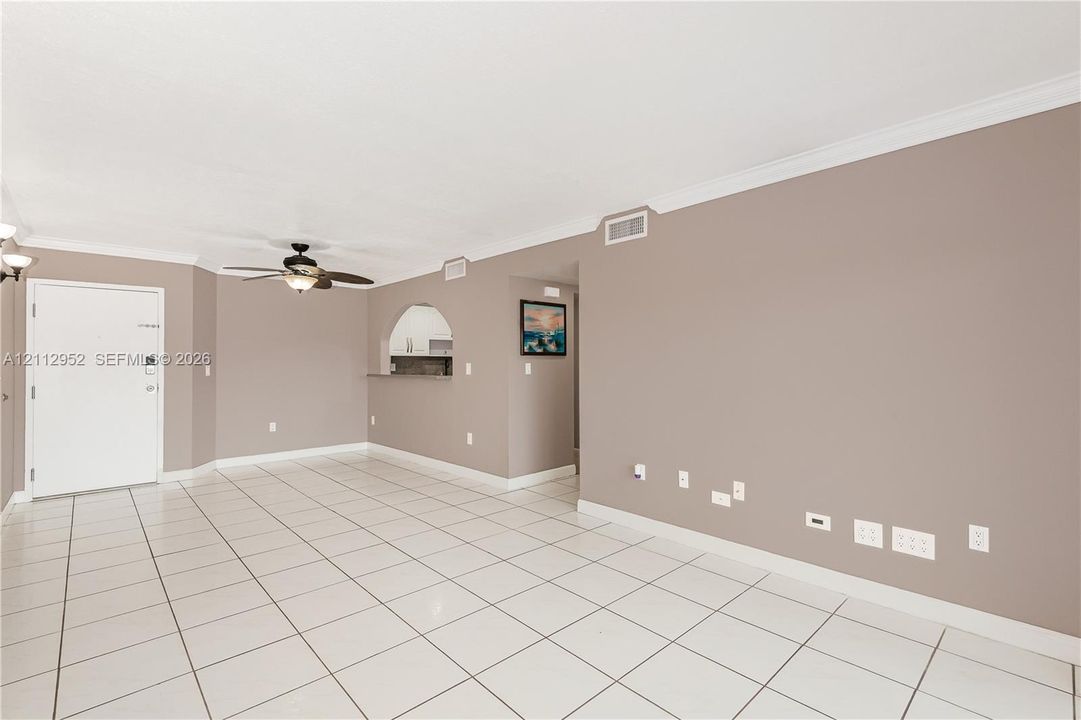 Neutral-toned interior featuring tiled flooring, crown molding, a ceiling fan with integrated light fixture, and an arched wall opening