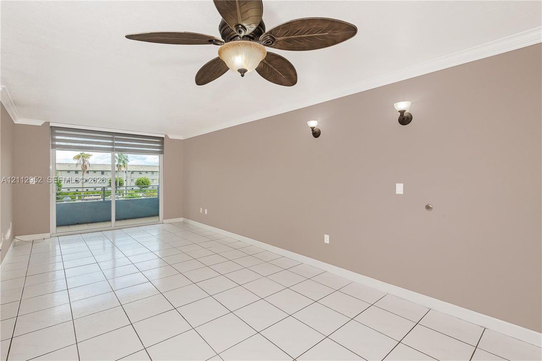 Interior space featuring large-format ceramic floor tiles, crown molding, a multi-blade ceiling fan with integrated light, dual wall-mounted sconces, and a sliding glass door providing external access