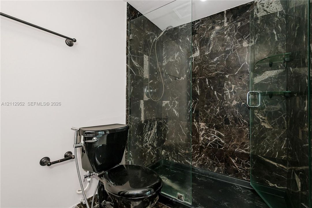Walk-in shower with dark veined stone surround, frameless glass enclosure, black plumbing fixtures, and matching black toilet